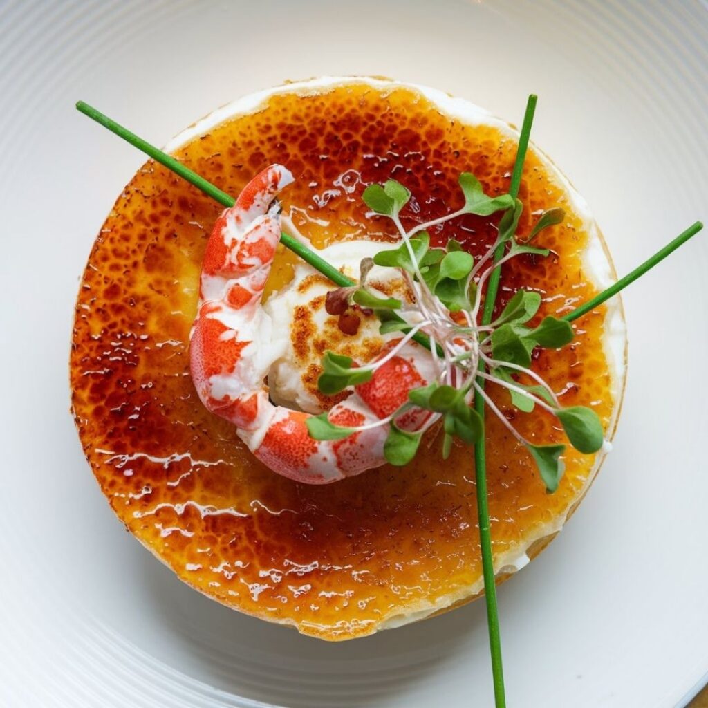 Overhead shot of crab brulee recipe with golden crust and green herb garnish