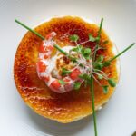 Overhead shot of crab brulee recipe with golden crust and green herb garnish