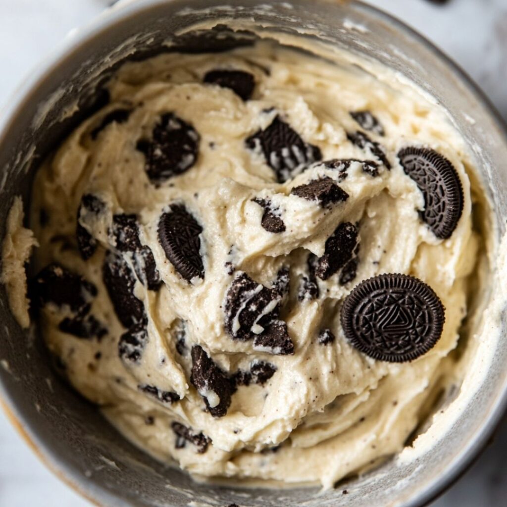 A mixing bowl filled with creamy cookie dough and chunks of Oreo cookies