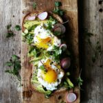 Overhead view of avocado toast with poached egg, microgreens, and radish slices on sourdough bread