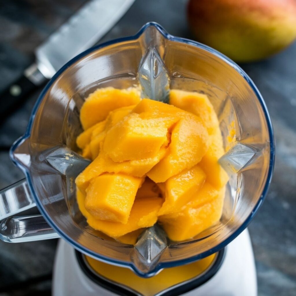 High-speed blender containing fresh mango puree in process, showing smooth texture and bright orange color